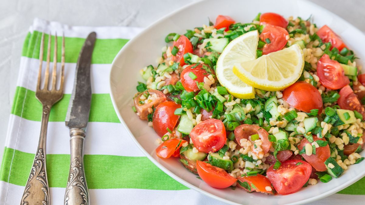 Tabbouleh freddo con farro, legumi misti, pomodorini e menta su sfondo rustico. Ricetta antispreco estiva della cucina ciociara.
